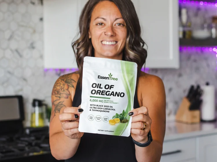 Sarah K. holding a pouch of EssenTree Oil of Oregano supplement in her kitchen