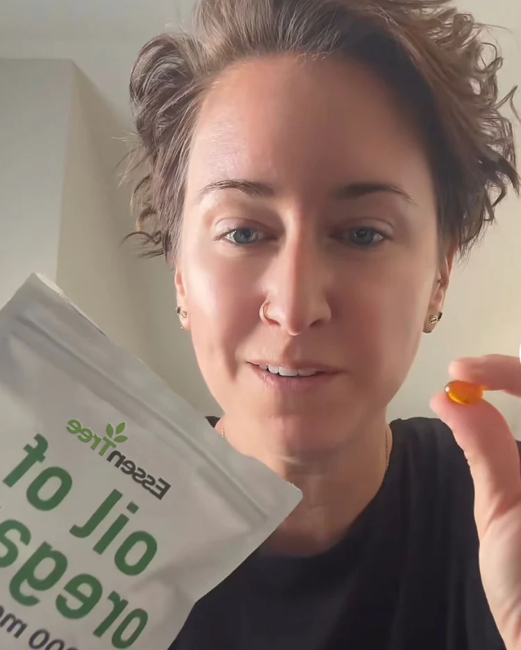 Kimberly R. holding a pouch of EssenTree Oil of Oregano supplement, showing a softgel capsule